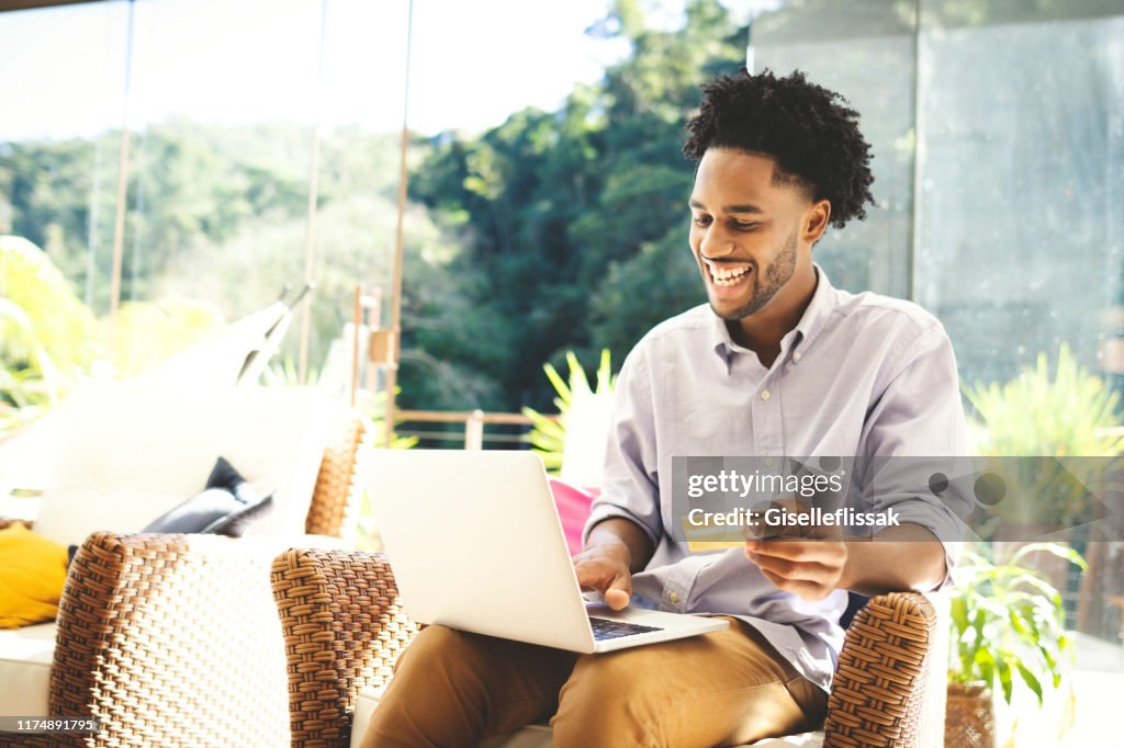 Young man using laptop, cell phone and credit card