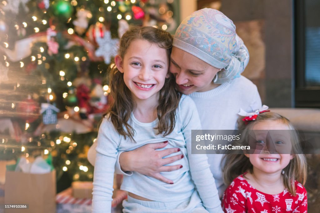 A beautiful mom battling cancer snuggles with her two daughters by the Christmas tree