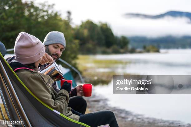 man and women drinking coffee by the lake in camping in autumn - fall camping stock pictures, royalty-free photos & images