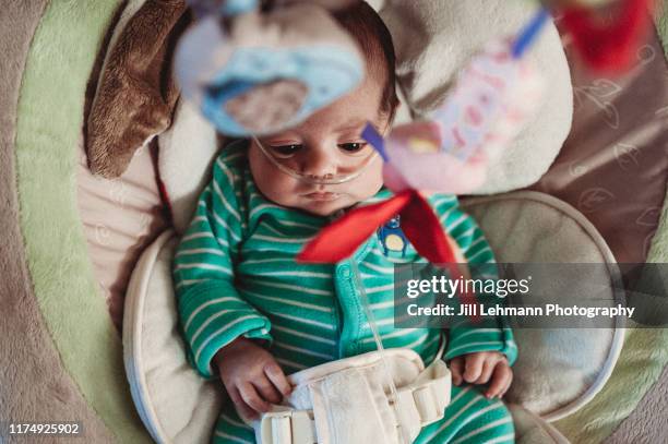 baby wearing nasal canula and oxygen relaxes at home in a chair - nasal cannula stock pictures, royalty-free photos & images