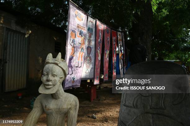 Craftsman exhibits a traditional mask and batik print textiles in a street in Bobo Dioulasso on September 18, 2019. - Warnings are handed out by...