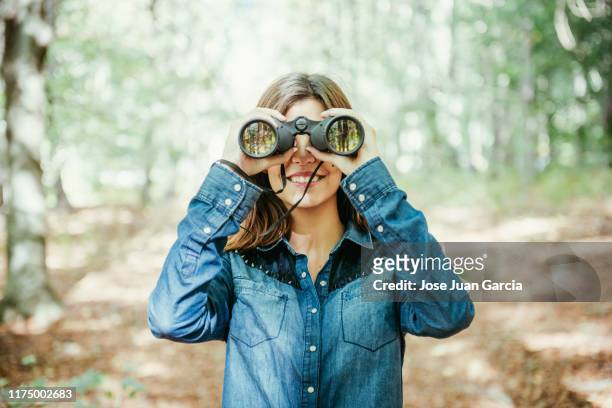 trendy young woman using binoculars in the woods - binoculars imagens e fotografias de stock
