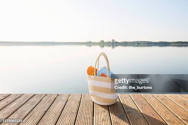 beach bag on a jetty at an idyllic lake with smooth water in the morning, tranquil scene - boardwalk stock pictures, royalty-free photos & images