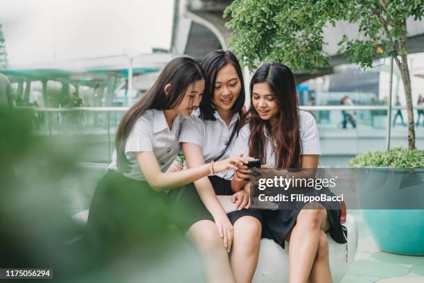 tres amigos estudiantes usando un teléfono móvil juntos en la ciudad - thai ethnicity fotografías e imágenes de stock