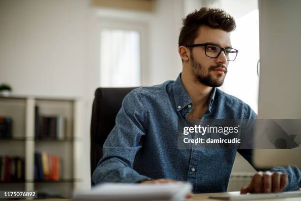 jeune homme travaillant dans le bureau - ordinateur personnel photos et images de collection