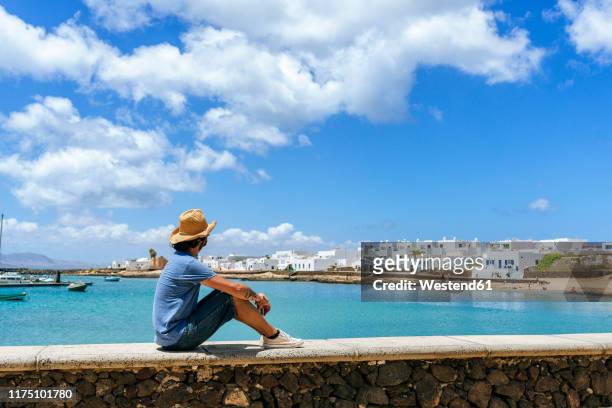 man sitting on wall looking towards caleta de sebo, la graciosa, canary islands, spain - lanzarote stockfoto's en -beelden