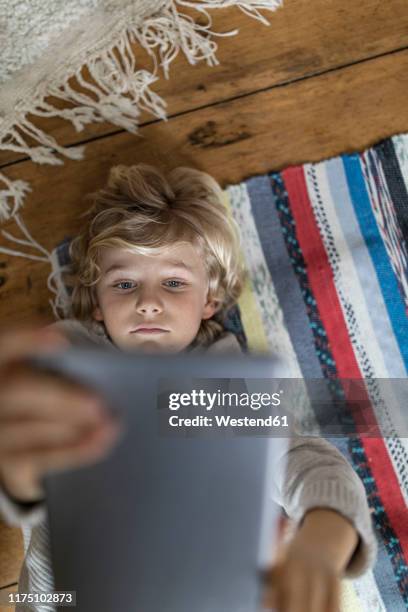 top view of boy lying on carpet using tablet - hochhalten stock-fotos und bilder