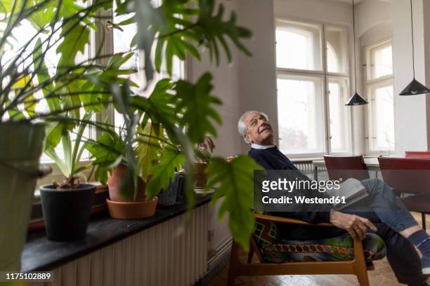 senior man sitting on chair at home - om zich heen kijken stockfoto's en -beelden