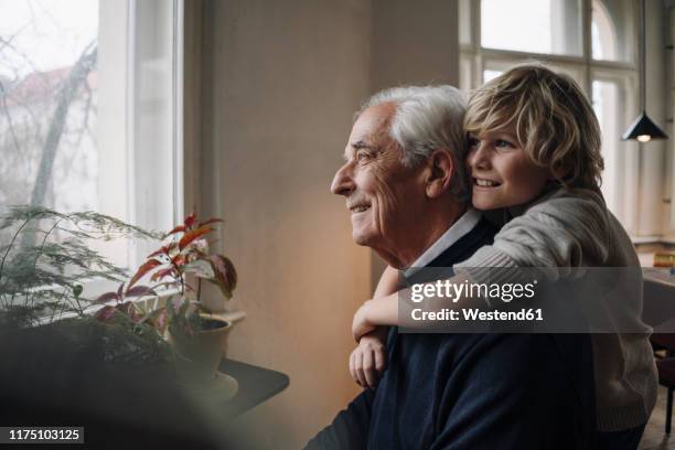 happy grandson embracing grandfather at home - alt und jung stock-fotos und bilder