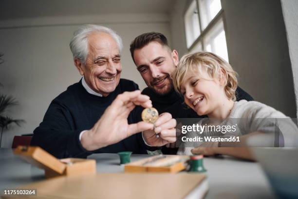 happy watchmaker showing clockwork to young man and boy - learning generation parent child photos et images de collection