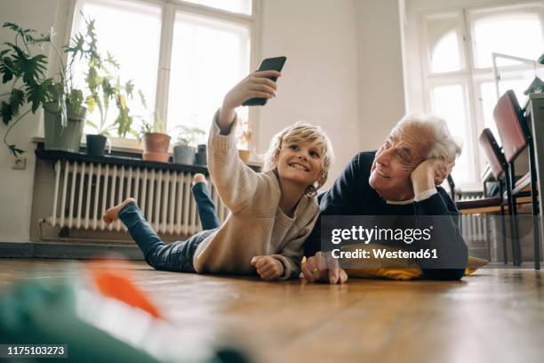 grandfather and grandson lying on the floor at home taking a selfie - enkelkind stock-fotos und bilder