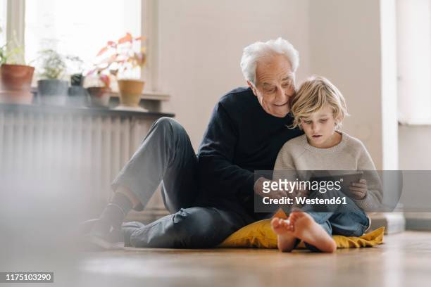 grandfather and grandson sitting on the floor at home using a tablet - sitting on floor fotografías e imágenes de stock