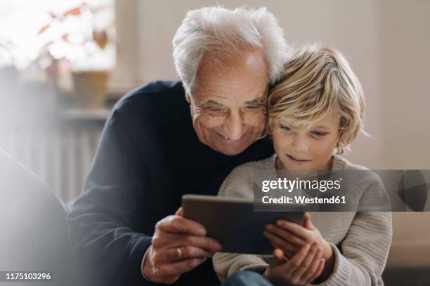 grandfather and grandson using a tablet at home - media availability stock-fotos und bilder