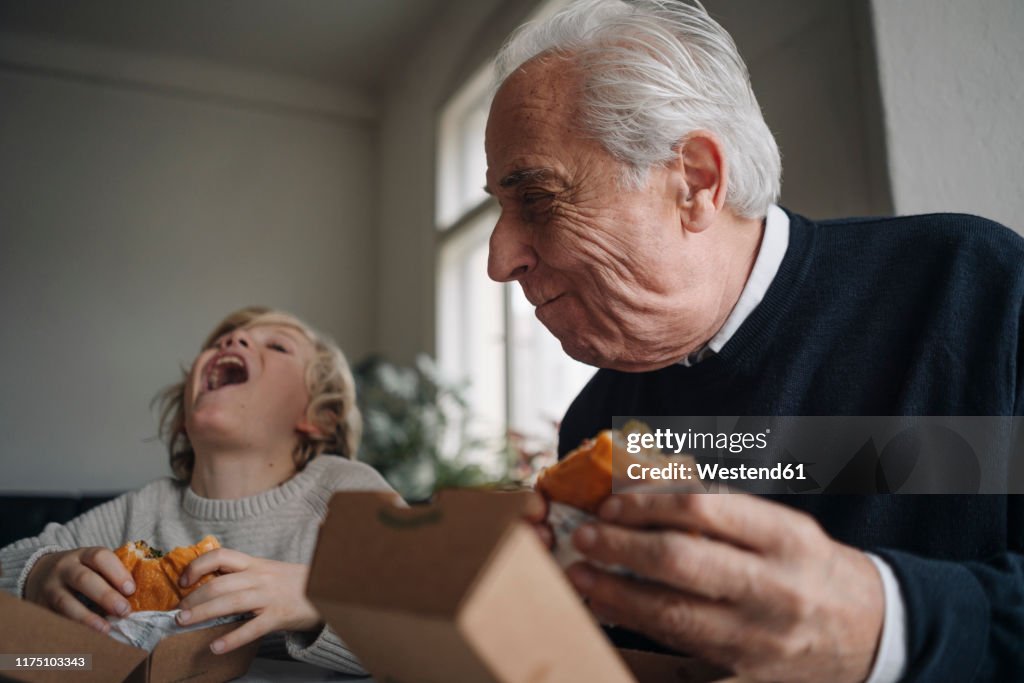 Happy grandfather and grandson eating burger together at home