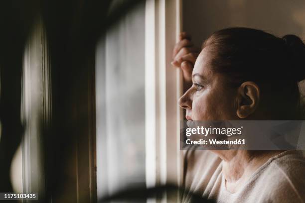 serious senior woman looking out of window at home - trauerzeit stock-fotos und bilder