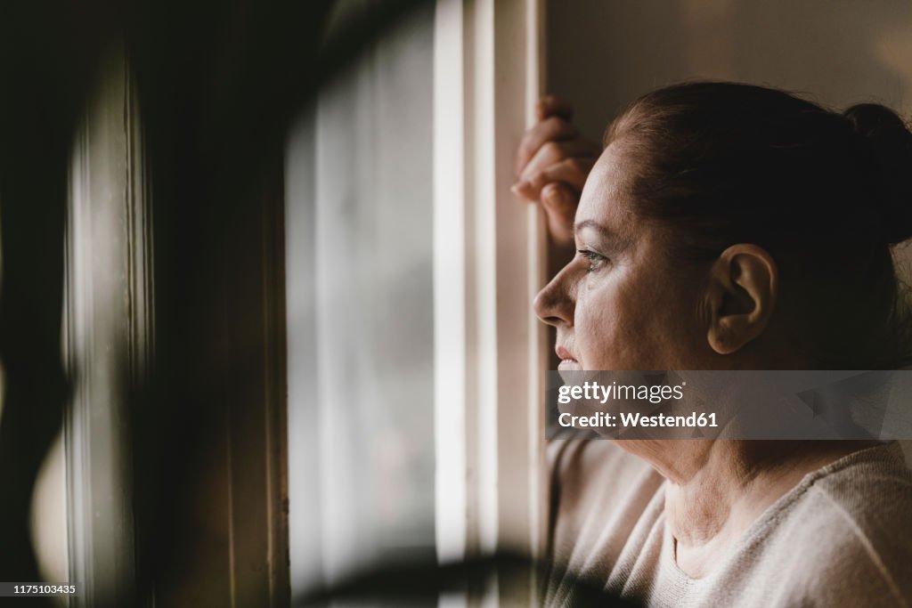 Serious senior woman looking out of window at home