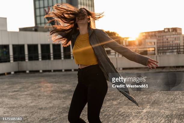 cheerful young woman dancing on parking deck at sunset - freiheit stock-fotos und bilder