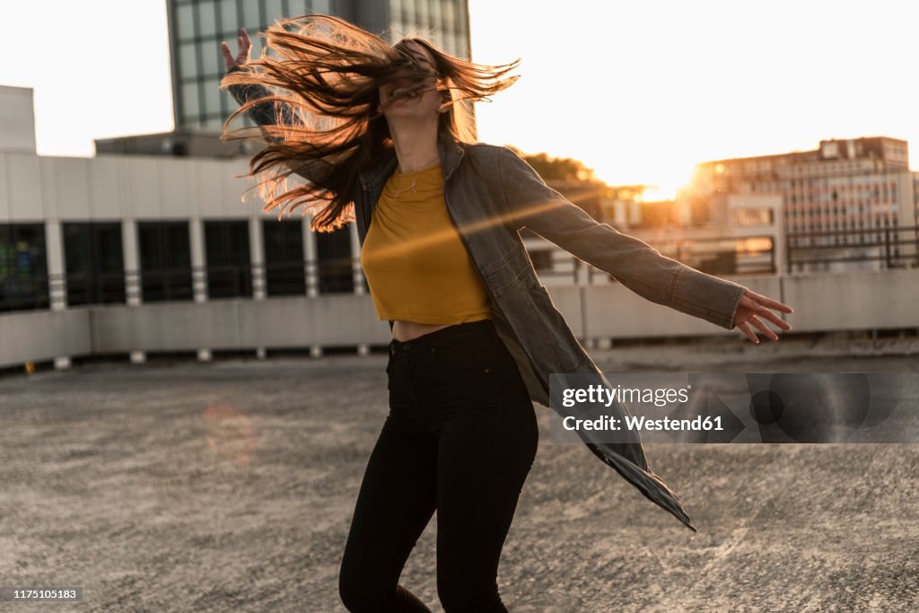 Cheerful young woman dancing on parking deck at sunset
