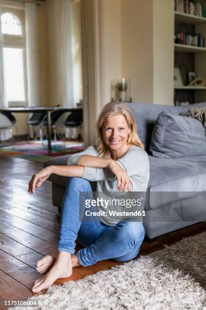 portrait of smiling mature woman siiting barefoot on the floor in the living room - human knee stock pictures, royalty-free photos & images