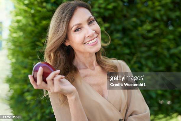 portrait of mature woman holding an apple, hedge in the background - apple fruit white background stock pictures, royalty-free photos & images