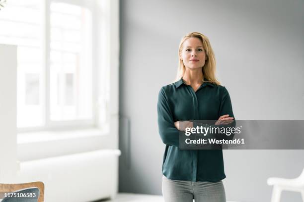 successful, blond businesswoman standing in bright room, with arms crossed - portrait of young woman standing against steps stockfoto's en -beelden