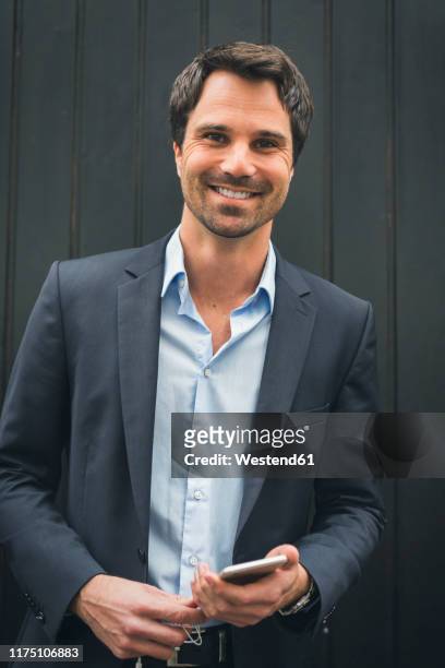 portrait of smiling businessman with mobile phone - gray jacket fotografías e imágenes de stock