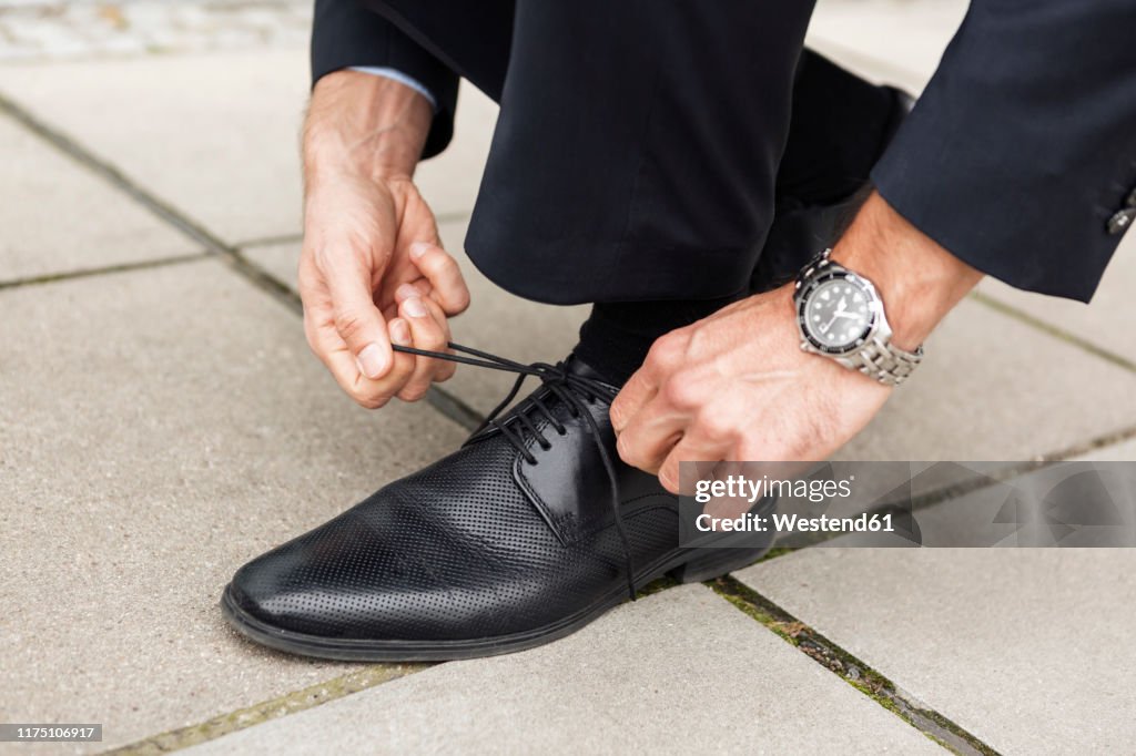 Businessman tying his shoe on pavement, close-up