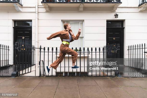 carefree young woman jumping in front of city houses, london, uk - running midair stock pictures, royalty-free photos & images