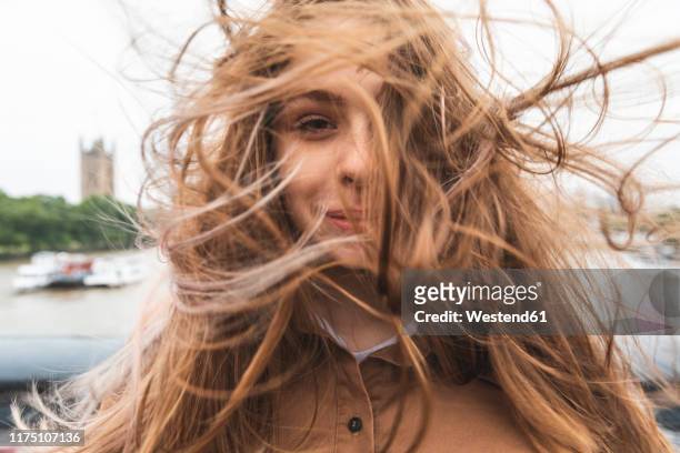 portrait of smiling young woman with windswept hair, london, uk - hair blowing stockfoto's en -beelden