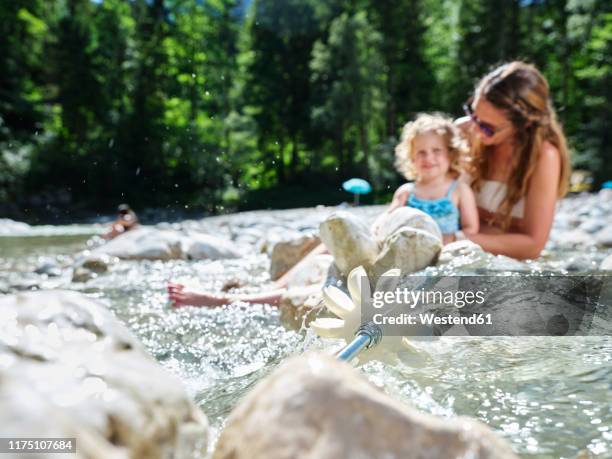 water wheel in a mountain stream with mother and daughter in background - wasserrad stock-fotos und bilder