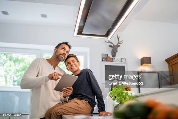 father and son using tablet in kitchen - kitchen straighten stockfoto's en -beelden