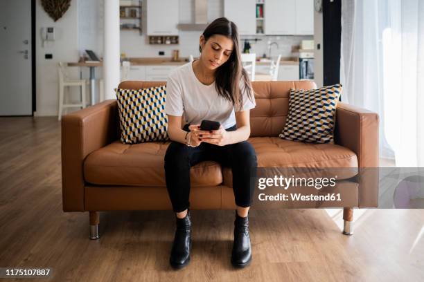 young woman on couch at home using cell phone - cushion photos et images de collection