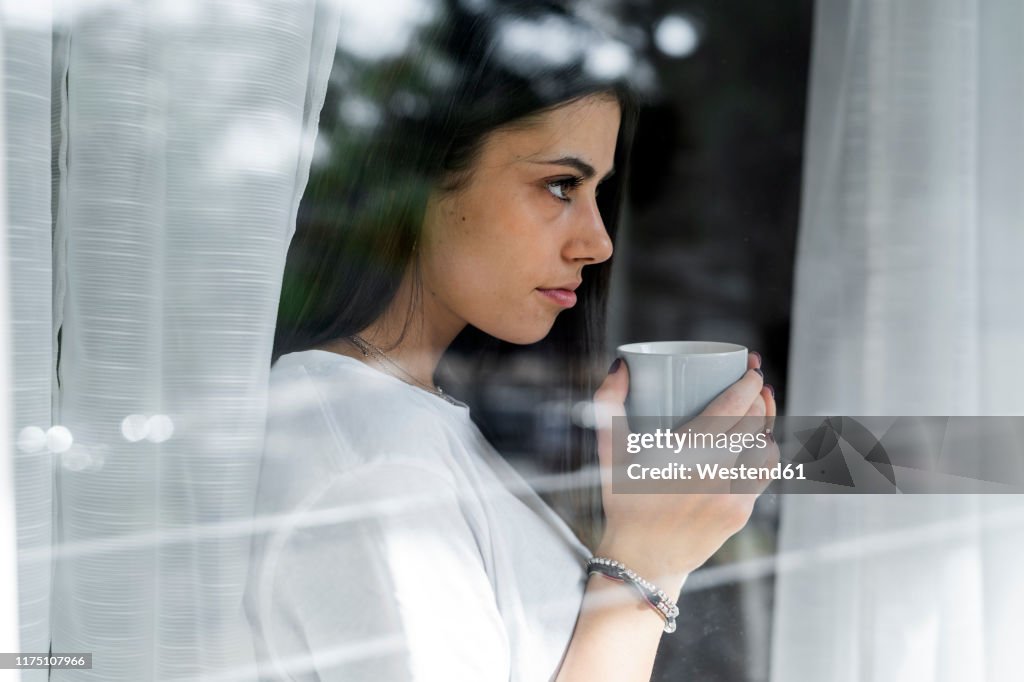 Young woman with cup of coffee behind windowpane