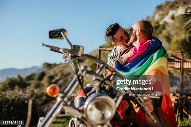 gay couple with gay pride flag kissing on a motorbike - gay flag stockfoto's en -beelden