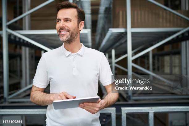 smiling man using tablet in a factory - camisa de polo fotografías e imágenes de stock