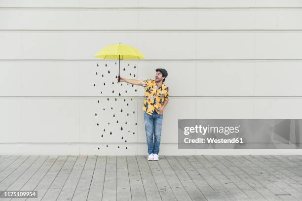 digital composite of young man holding an umbrella at a wall with raindrops - man with umbrella stockfoto's en -beelden