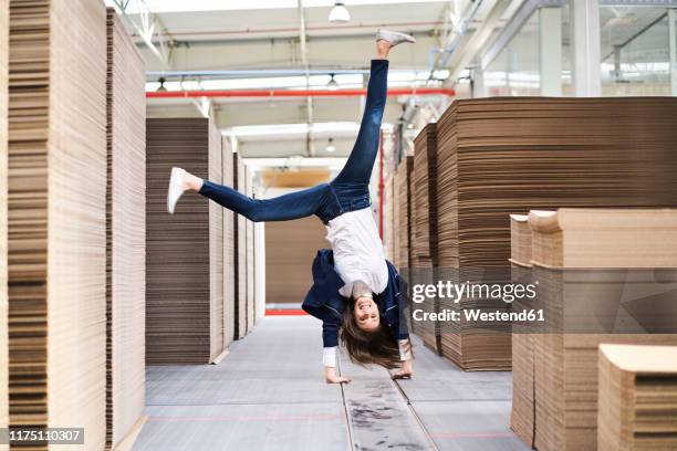 excited businesswoman doing a handstand in factory warehouse - businesswoman handstand stock-fotos und bilder