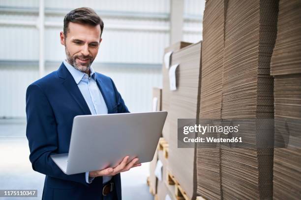 businessman using laptop in a factory warehouse - business man holding stock-fotos und bilder