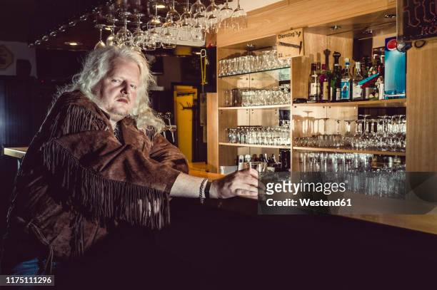portrait of blond rocker wearing brown leather jacket standing at counter of an old-fashioned pub - bar stock-fotos und bilder