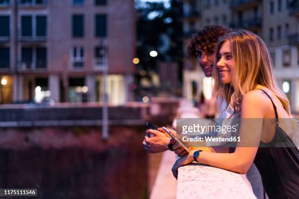 happy young couple leaning on bridge railing at night, verona, italy - verona italy stock-fotos und bilder