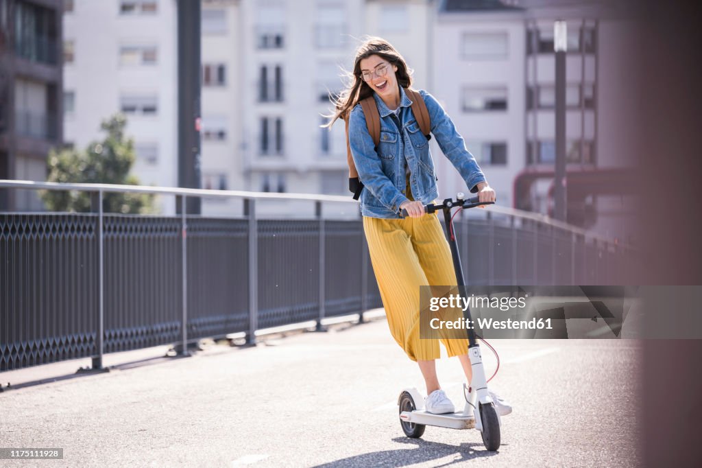 Happy young woman riding electric scooter on a bridge