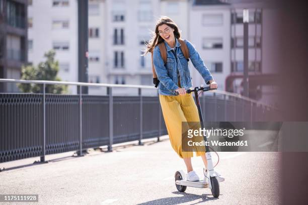happy young woman riding electric scooter on a bridge - active lifestyle stock-fotos und bilder
