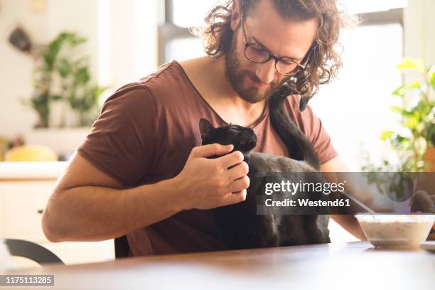 young man stroking his black cat at home - cat owner stock pictures, royalty-free photos & images