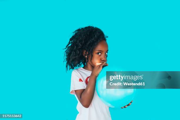 little girl in front of a blue wall, blowing up balloon - child balloon studio photos et images de collection