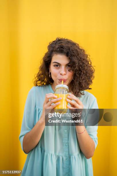 portrait of woman drinking juice, yellow background - orange juice glass white background stock pictures, royalty-free photos & images