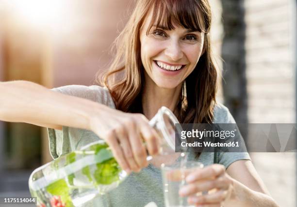 portrait of happy woman pouring infused water into glass - infused water stockfoto's en -beelden