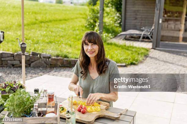 portrait of smiling woman preparing a salad on garden table - gelbe paprika stock-fotos und bilder