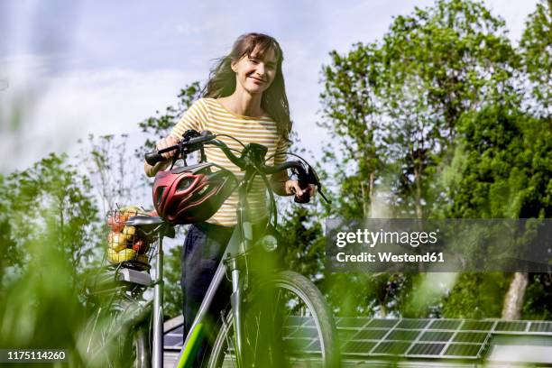 smiling woman pushing bicycle with organic fruit on a meadow - apple building stock-fotos und bilder