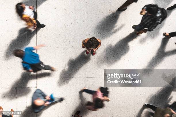 woman looking at mobile phone in between hurrying people, top view - persona in secondo piano foto e immagini stock