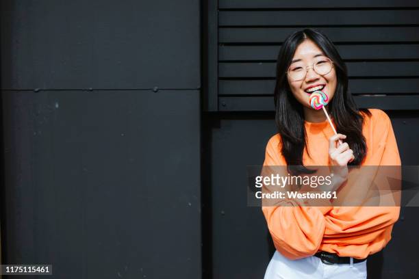 young asian woman with lollipop in front of black wall - asian hair stock-fotos und bilder